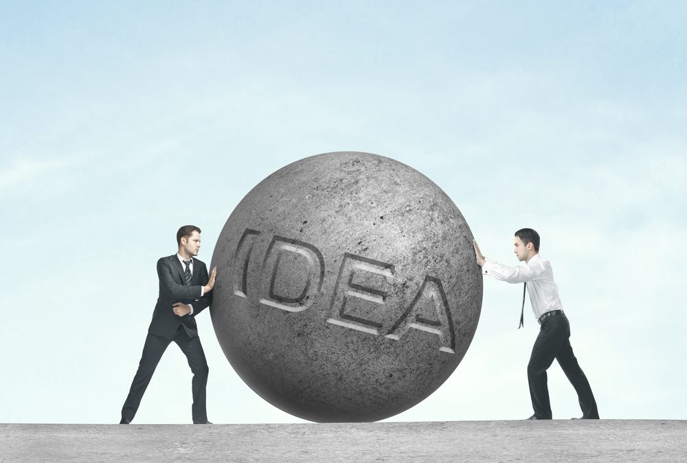 two people pushing a stone with the word 'idea' written on it