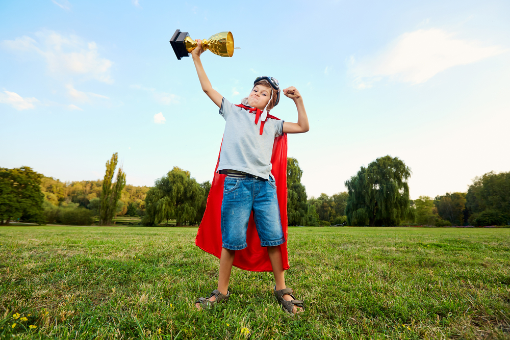 Kid wearing a cape holding a giant trophy