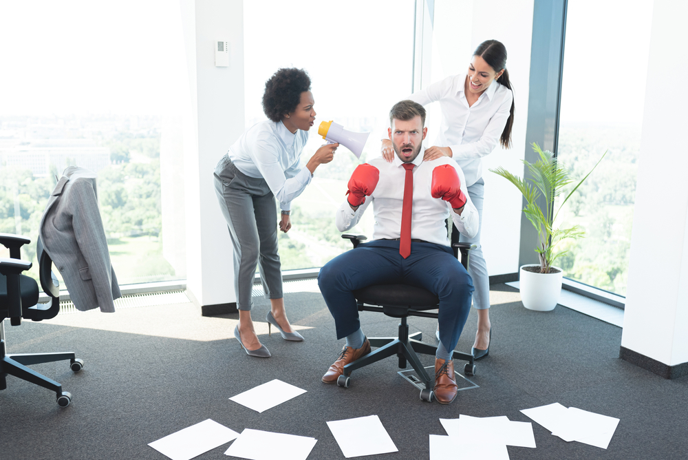 Business man wearing boxing gloves while female colleagues encourage him to fight