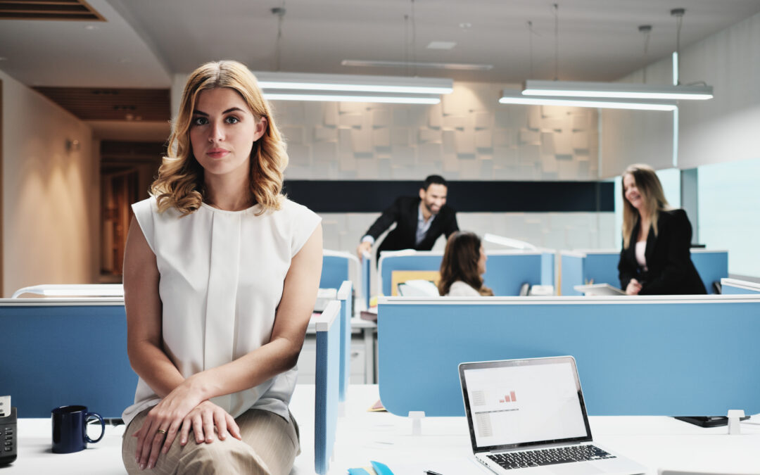 Woman sitting on desk alone while teammate talk without her
