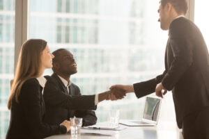 Person standing, shaking hands with people already at a meeting