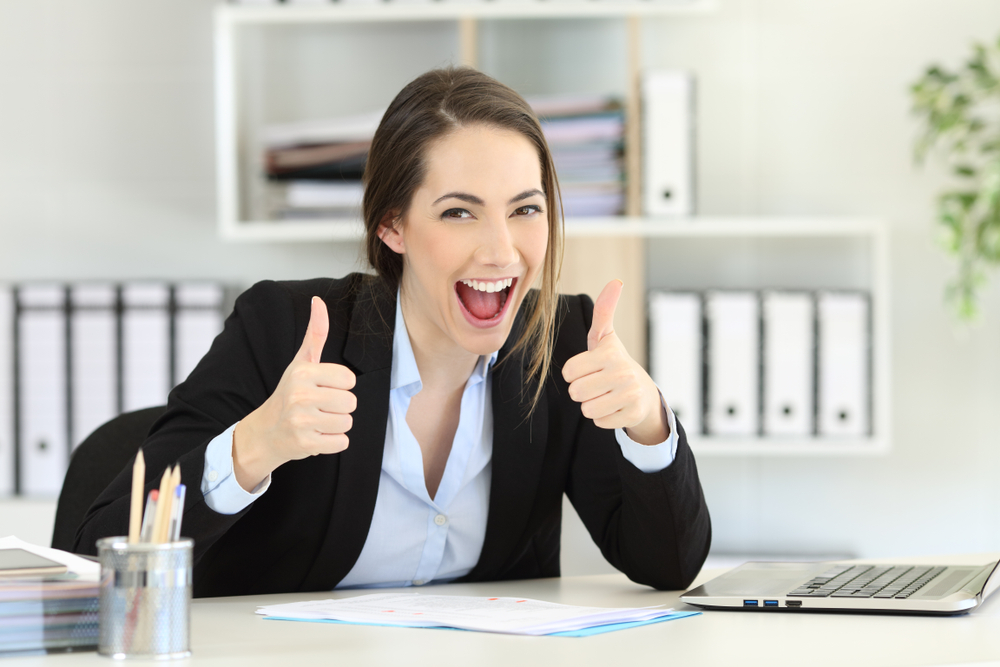 Woman at desk giving enthusiastic two thumbs up