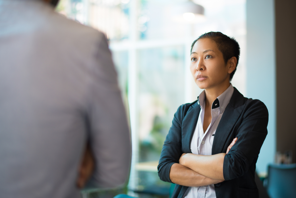 Woman with arms crossed looking dubious while talking to a colleague