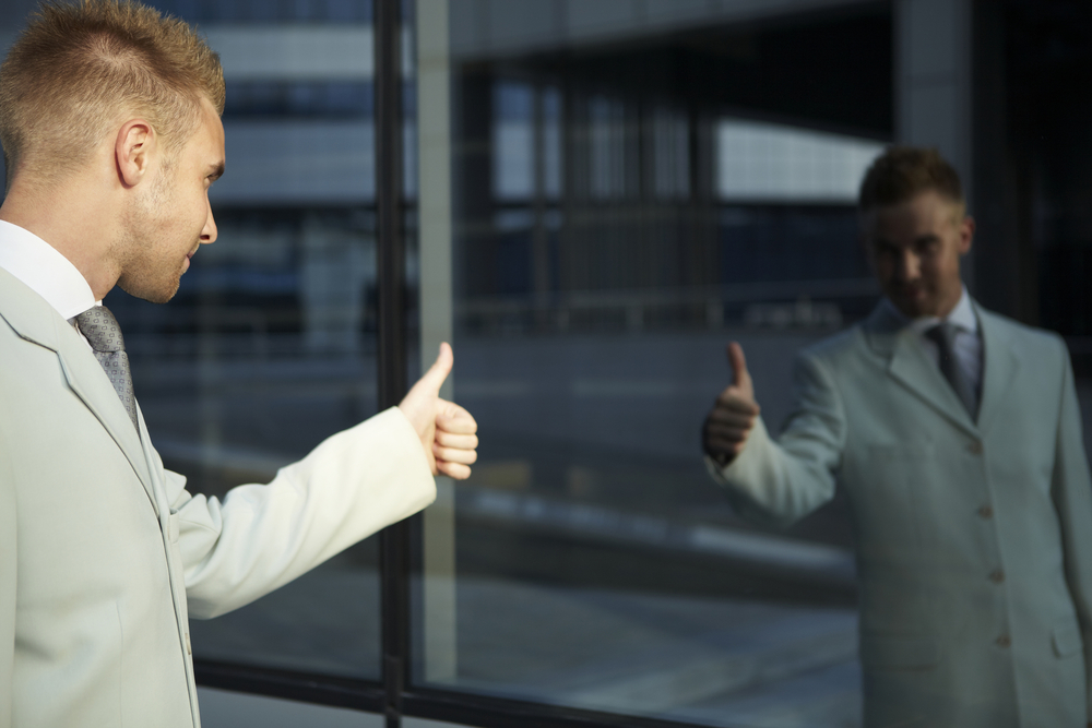 Man looking at reflection in a window and giving himself a thumbs up